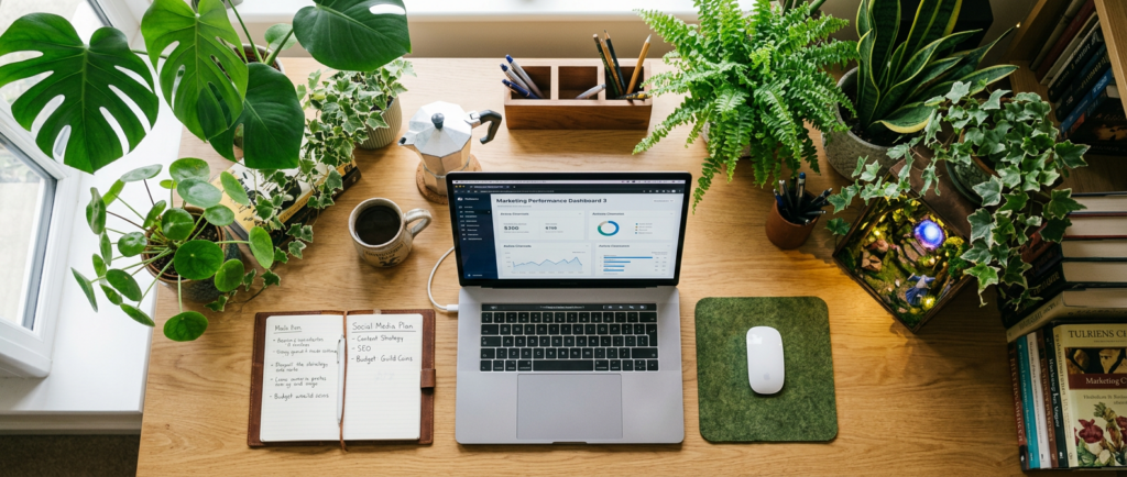 Woman working on laptop at desk filled with houseplants and personal items